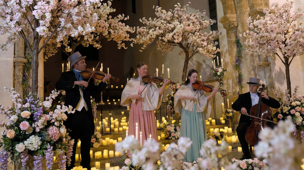 Musicians playing string instruments in a decorated indoor setting with flowers and candles.